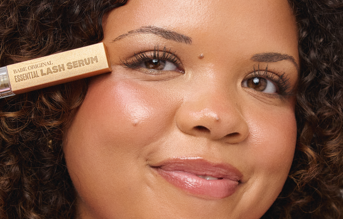 Model holding Essential Lash Serum showing natural long lashes